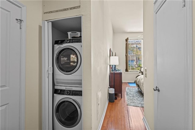 laundry room featuring laundry area, stacked washing maching and dryer, baseboards, and wood finished floors