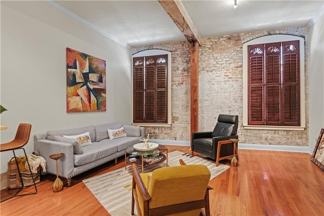 living area featuring wood finished floors, baseboards, brick wall, beam ceiling, and ornamental molding