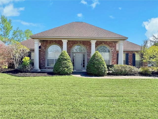 neoclassical home with a front yard, brick siding, and a shingled roof