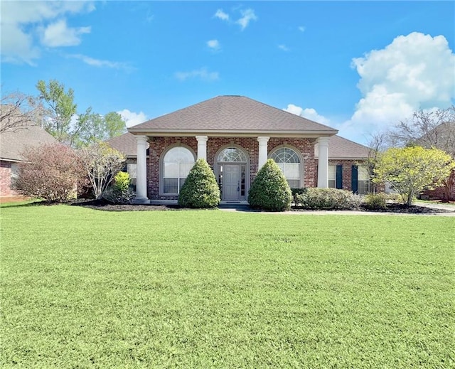 greek revival inspired property with a front yard, brick siding, and a shingled roof