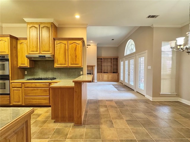 kitchen featuring visible vents, ornamental molding, light countertops, under cabinet range hood, and backsplash