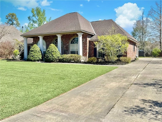 neoclassical home featuring a front lawn, concrete driveway, brick siding, and a shingled roof