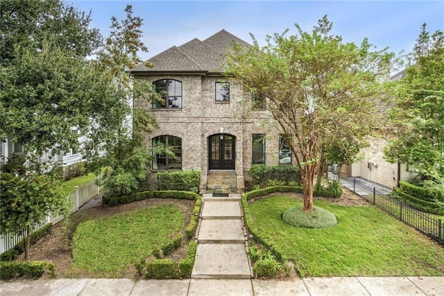 french country inspired facade featuring brick siding, a fenced backyard, a front yard, and a shingled roof