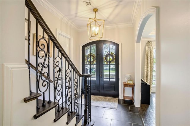 foyer entrance featuring visible vents, a chandelier, stairs, ornamental molding, and arched walkways