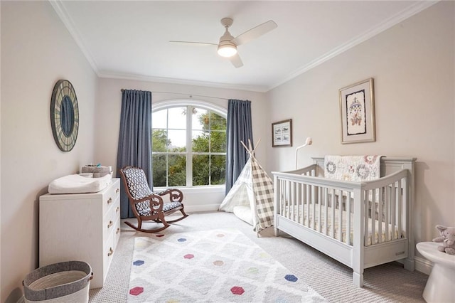 bedroom with ceiling fan, baseboards, ornamental molding, carpet flooring, and a nursery area