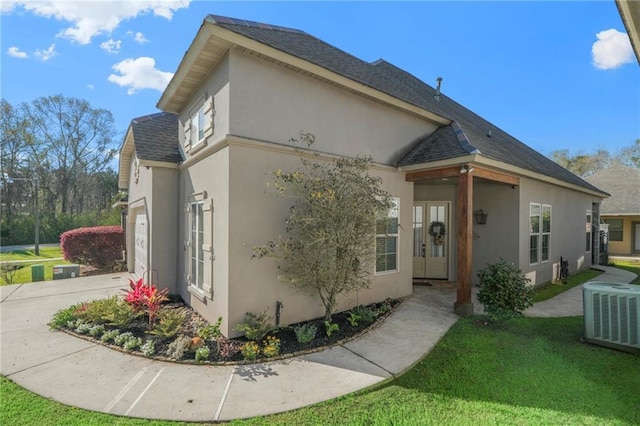 view of front of property featuring a shingled roof, central air condition unit, a front yard, stucco siding, and driveway