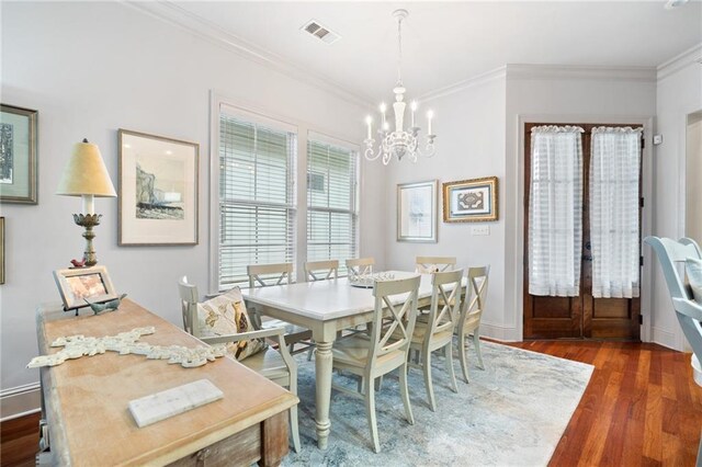 dining space featuring an inviting chandelier, wood finished floors, visible vents, and ornamental molding