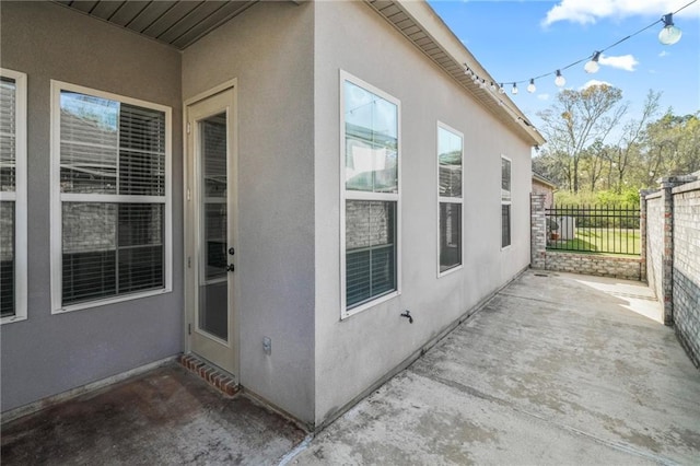 view of side of home with stucco siding, a patio, and fence