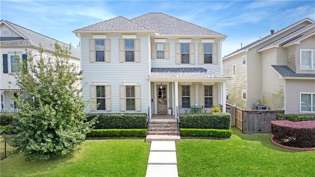 view of front of house with a porch, fence, a front lawn, and a shingled roof