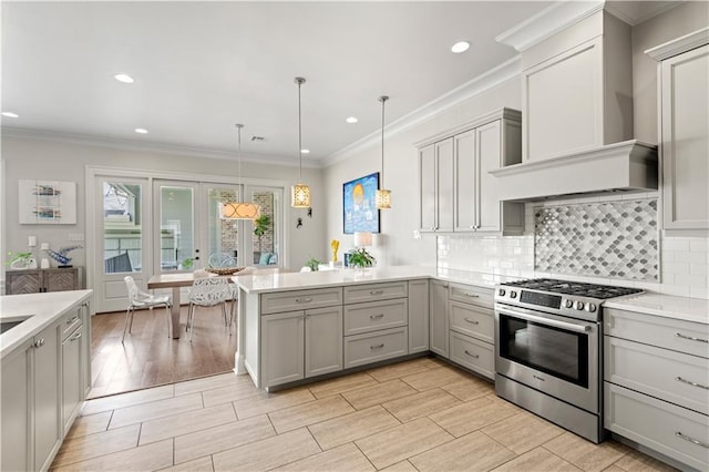 kitchen featuring stainless steel gas range, a peninsula, gray cabinets, light countertops, and wall chimney range hood