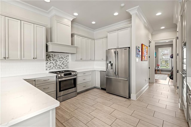 kitchen with wood finish floors, light stone counters, stainless steel appliances, wall chimney range hood, and decorative backsplash