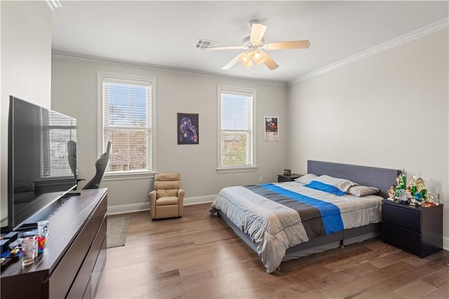 bedroom with visible vents, light wood-style flooring, a ceiling fan, ornamental molding, and baseboards