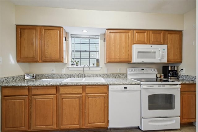 kitchen with light stone countertops, white appliances, brown cabinets, and a sink