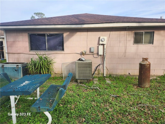 back of property featuring cooling unit and roof with shingles