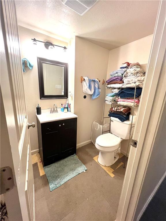 half bathroom featuring vanity, toilet, baseboards, and a textured ceiling
