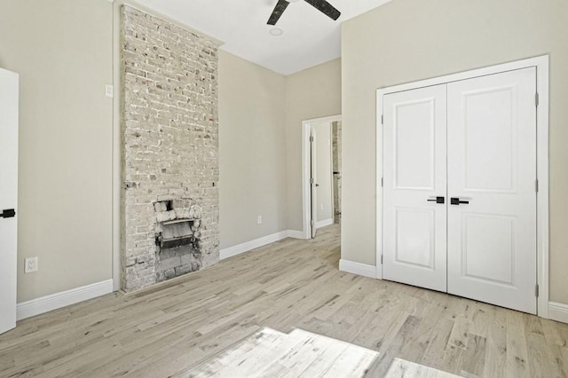 unfurnished living room featuring baseboards, a large fireplace, ceiling fan, and wood finished floors
