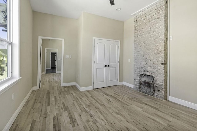 unfurnished living room featuring baseboards, a stone fireplace, light wood-style flooring, and a towering ceiling