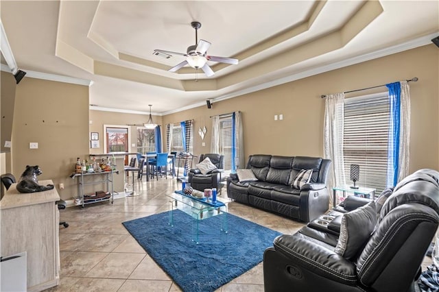 living area featuring a tray ceiling, ornamental molding, light tile patterned floors, and ceiling fan