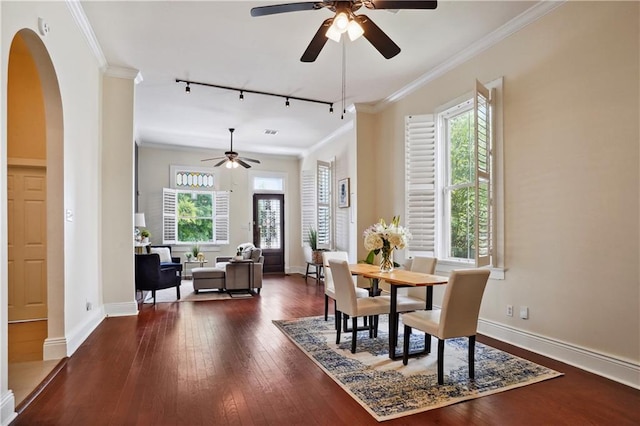 dining space featuring dark wood finished floors, crown molding, a ceiling fan, and arched walkways