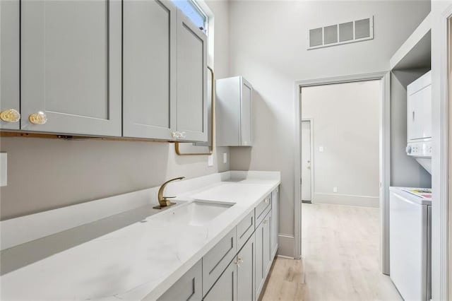 washroom with visible vents, stacked washer and clothes dryer, light wood-style floors, baseboards, and a sink