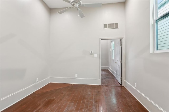 spare room featuring ceiling fan, a high ceiling, wood-type flooring, baseboards, and visible vents