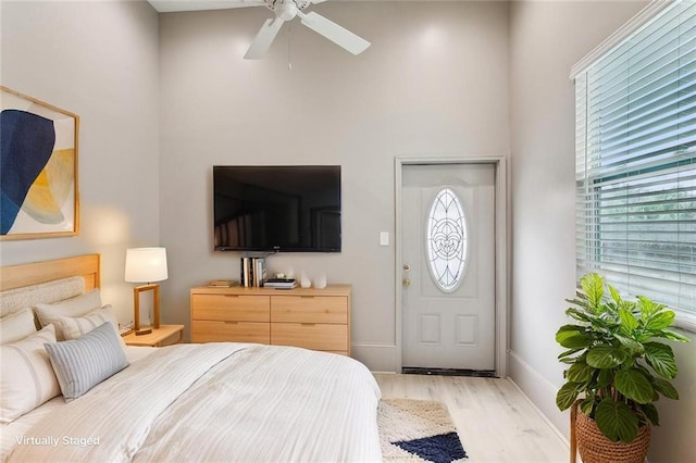 bedroom featuring light wood-type flooring, baseboards, ceiling fan, and a high ceiling