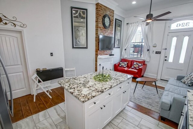 326 N Tonti St, New Orleans, LA 70119 - kitchen featuring light stone counters, ceiling fan, white cabinets, a center island, and light marble finish flooring