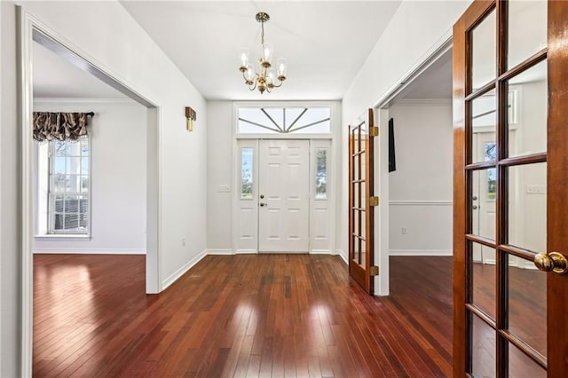 foyer entrance featuring a chandelier, dark wood-style floors, baseboards, and ornamental molding