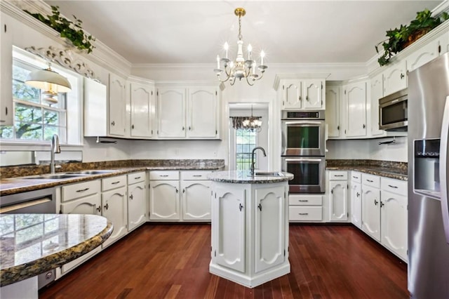 kitchen with a sink, stainless steel appliances, an inviting chandelier, and white cabinets