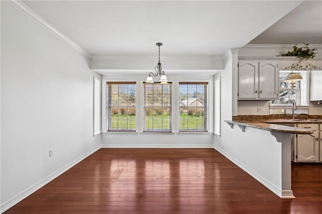 unfurnished dining area featuring crown molding, baseboards, dark wood finished floors, an inviting chandelier, and a sink