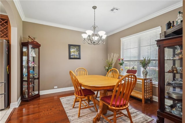 dining room featuring wood finished floors, visible vents, baseboards, ornamental molding, and a notable chandelier
