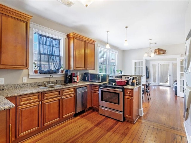 311214 General Taylor St, New Orleans, LA 70125 - kitchen featuring appliances with stainless steel finishes, light wood finished floors, brown cabinets, a peninsula, and light stone counters