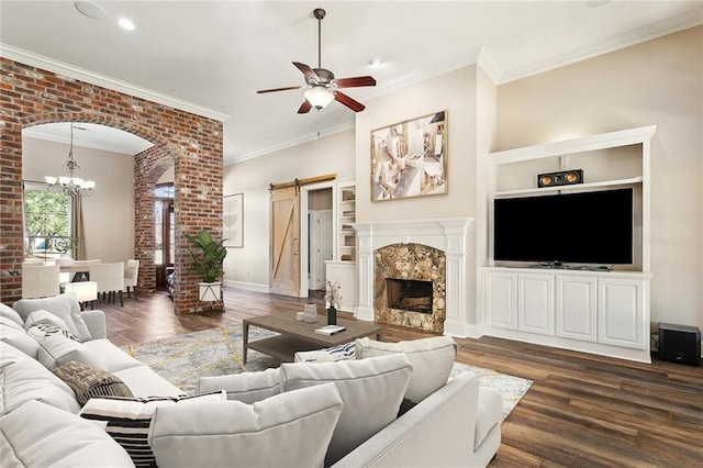 living area with ceiling fan with notable chandelier, a barn door, ornamental molding, and dark wood-type flooring