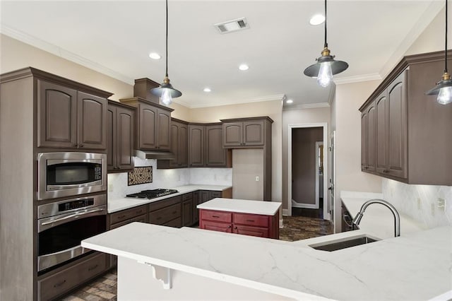 kitchen with crown molding, a sink, under cabinet range hood, stainless steel appliances, and visible vents