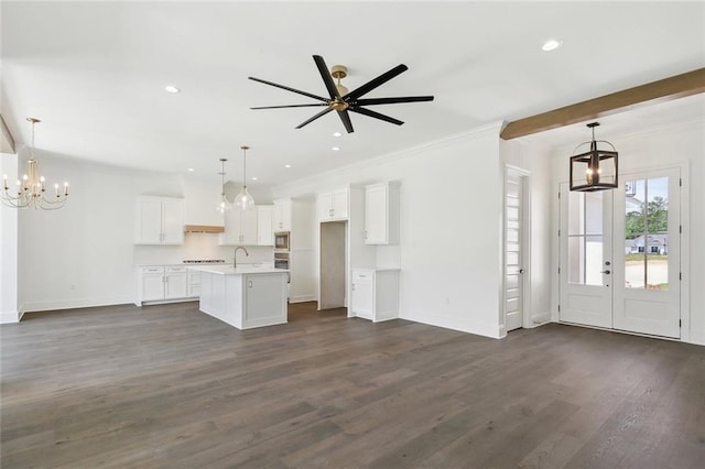 unfurnished living room featuring baseboards, ornamental molding, dark wood-type flooring, and ceiling fan with notable chandelier