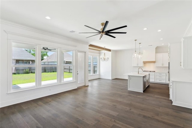 unfurnished living room with crown molding, dark wood-type flooring, ceiling fan with notable chandelier, and a healthy amount of sunlight
