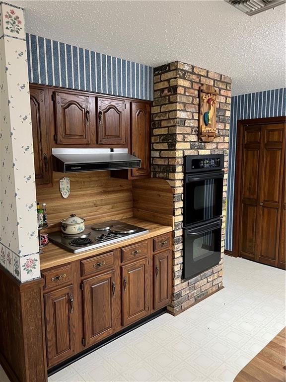 137 Nolan Dr, La Place, LA 70068 - kitchen featuring dobule oven black, stainless steel stovetop, a textured ceiling, under cabinet range hood, and wallpapered walls