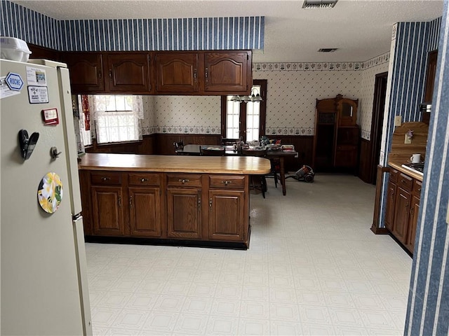 137 Nolan Dr, La Place, LA 70068 - kitchen featuring wallpapered walls, a textured ceiling, freestanding refrigerator, wainscoting, and light floors