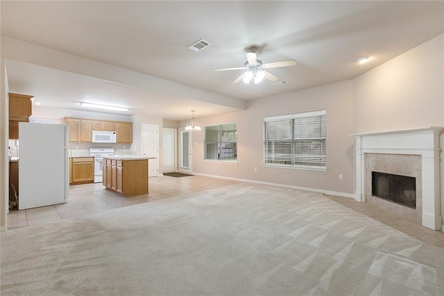 unfurnished living room featuring light tile patterned flooring, ceiling fan with notable chandelier, a high end fireplace, light colored carpet, and visible vents