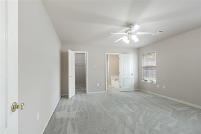 unfurnished bedroom with light colored carpet, a spacious closet, baseboards, a ceiling fan, and a closet