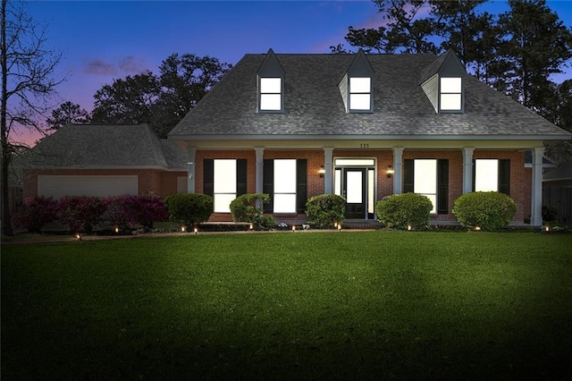 new england style home featuring a yard, brick siding, and roof with shingles