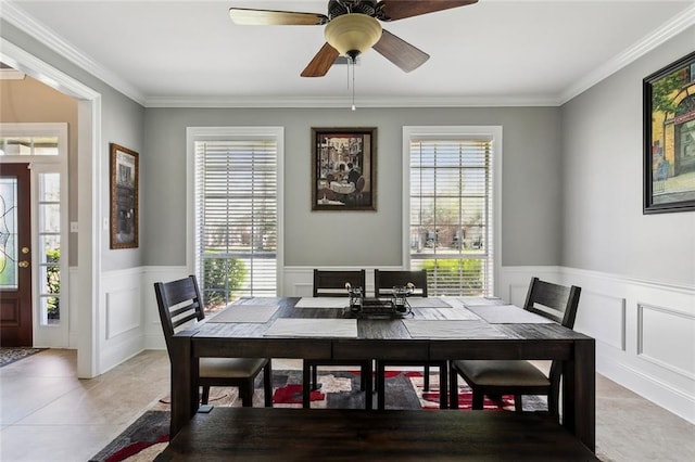 dining space with ornamental molding, a ceiling fan, light tile patterned flooring, and wainscoting