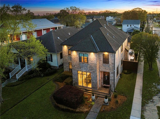 5878 General Haig St, New Orleans, LA 70124 - back of house at dusk with a shingled roof, a lawn, brick siding, and a residential view