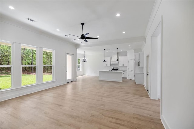 unfurnished living room with ceiling fan with notable chandelier, light wood-style flooring, ornamental molding, visible vents, and recessed lighting