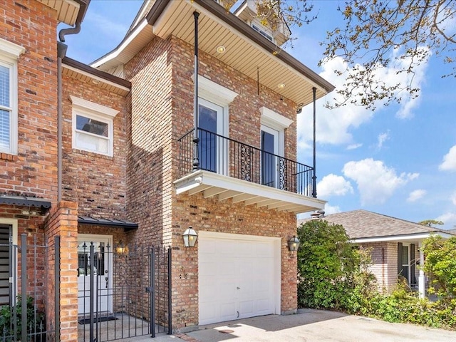 view of front of house with a garage, brick siding, a balcony, and driveway