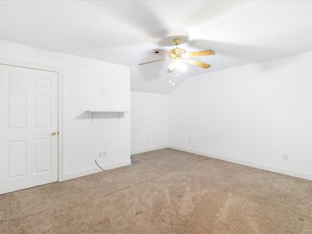 unfurnished room featuring ceiling fan, vaulted ceiling, baseboards, and light colored carpet
