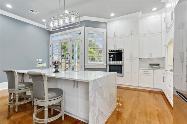 736 Belleville St, New Orleans, LA 70114 - kitchen featuring stainless steel double oven, white cabinets, recessed lighting, ornamental molding, and light wood-type flooring