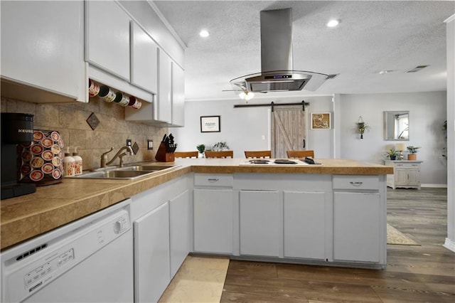kitchen featuring a barn door, a peninsula, island exhaust hood, white appliances, and a sink