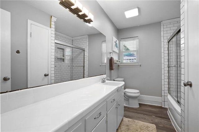 full bathroom with toilet, wood finished floors, baseboards, enclosed tub / shower combo, and vanity
