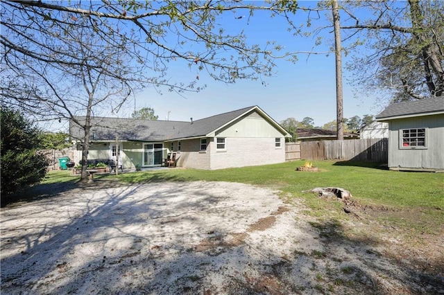 back of house featuring an outbuilding, a yard, a fenced backyard, and dirt driveway